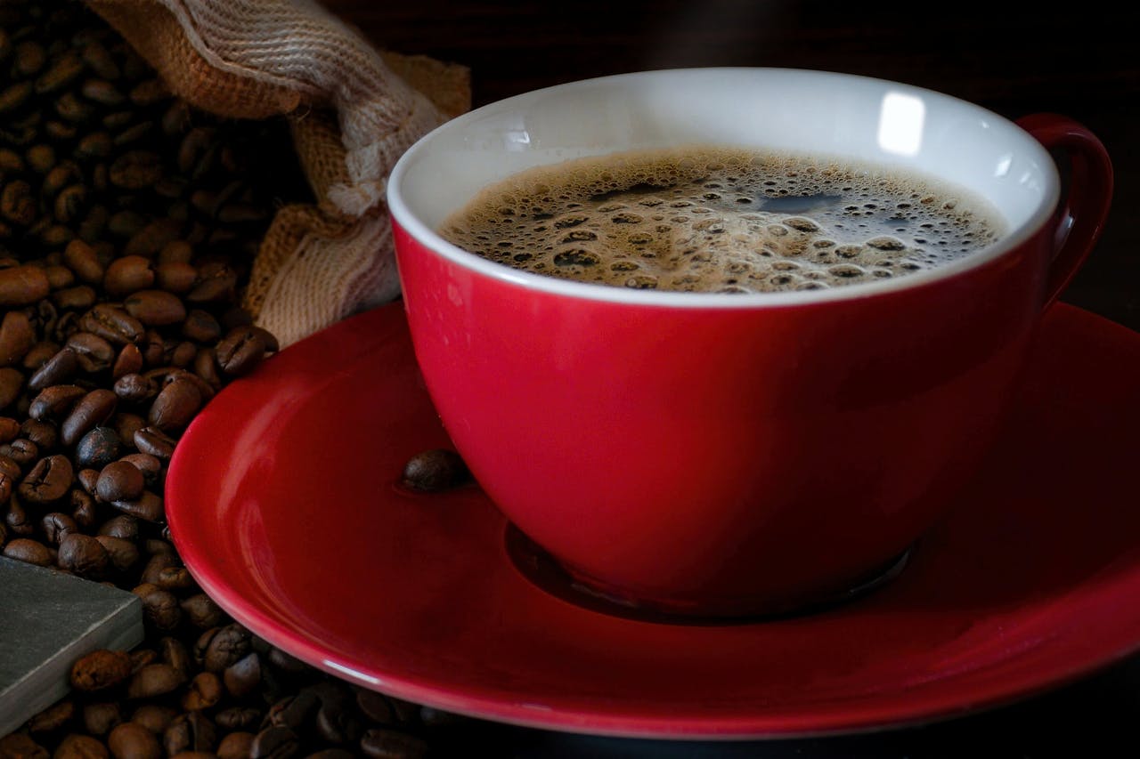 A steaming cup of espresso in a red mug surrounded by coffee beans. Perfect for morning routines.