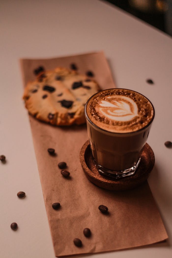 Aesthetic setup of a latte with latte art and a chocolate chip cookie on a wooden table, perfect for a cozy cafe theme.